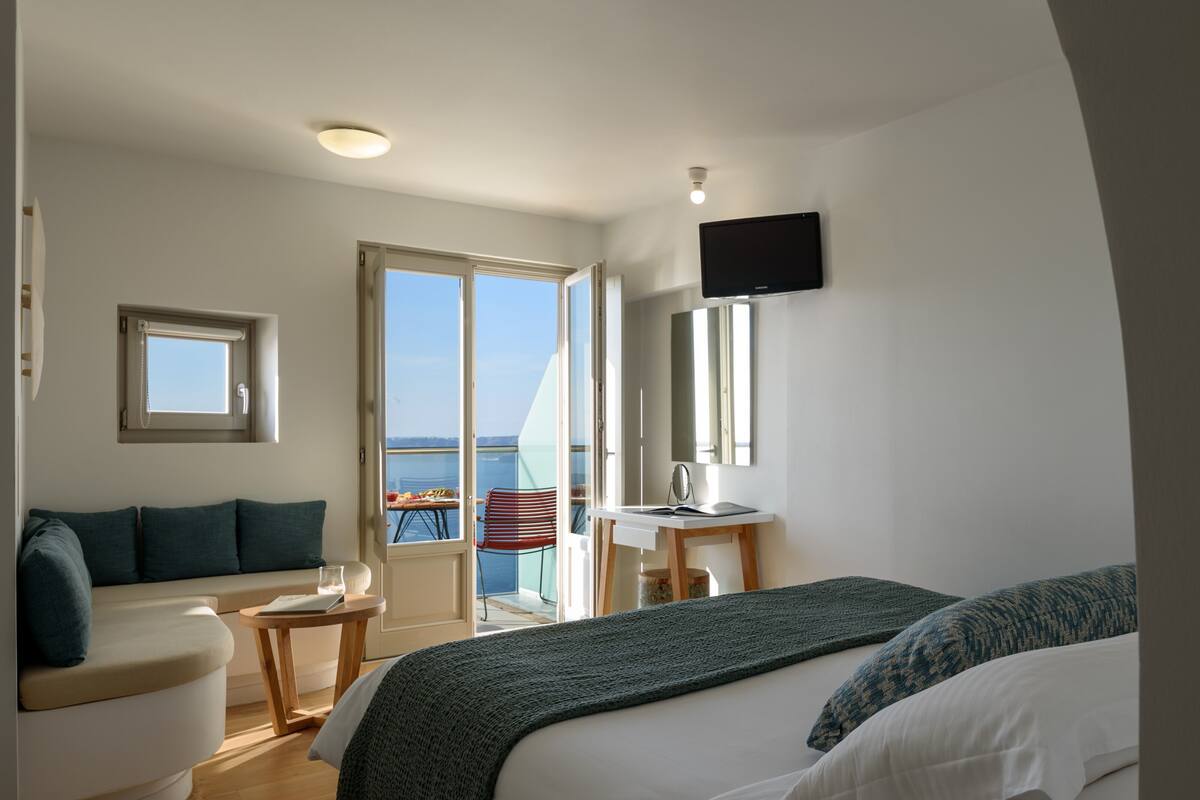 Moderni hotellihuone, jossa on suuri sänky, työpöytä, tuoli ja parveke, jolta on näkymä.