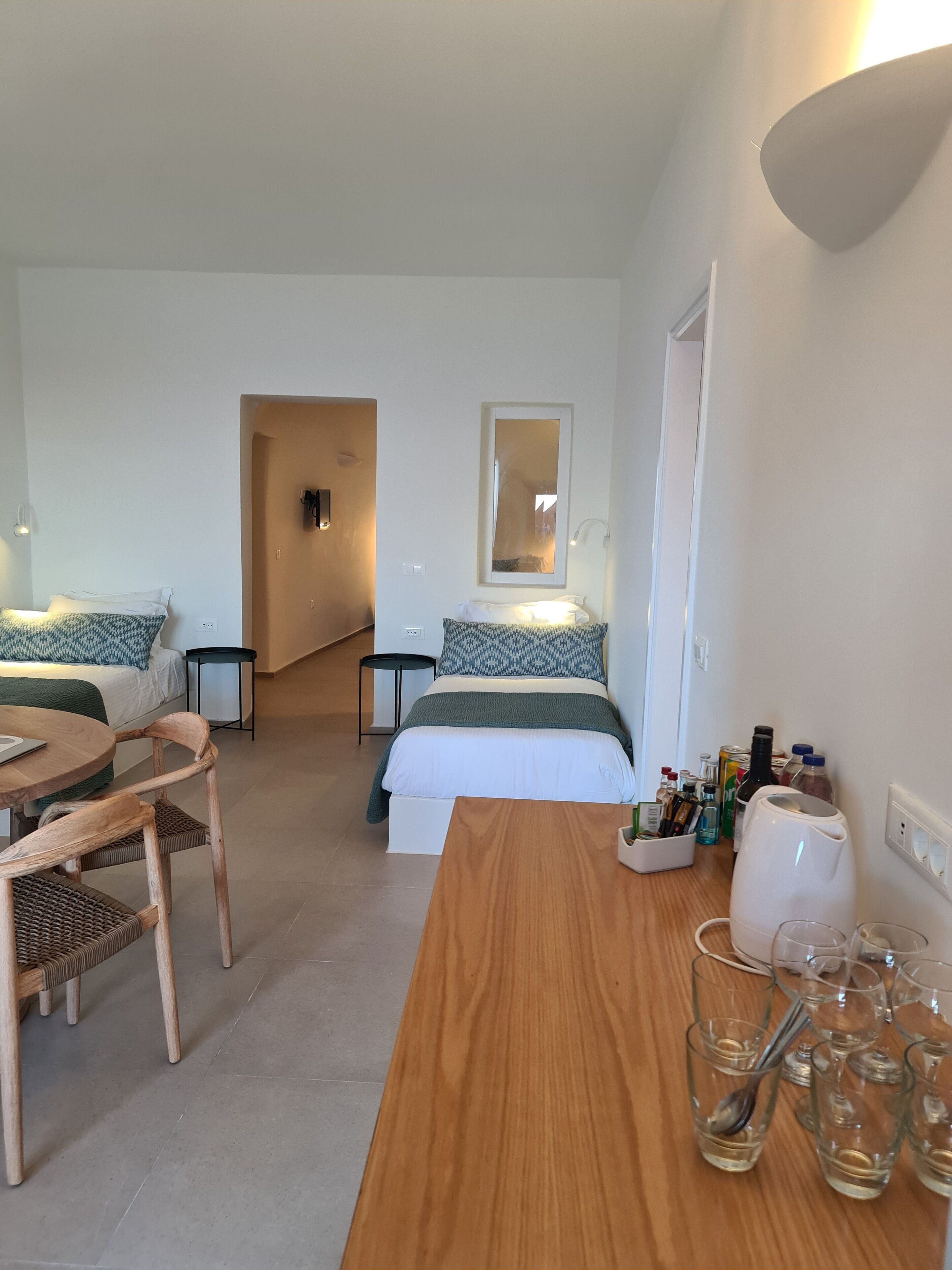 Habitación de hotel con cama, una mesa de madera y una zona de estar con sillas. Hay un espejo en la pared y una mesita con botellas y vasos.