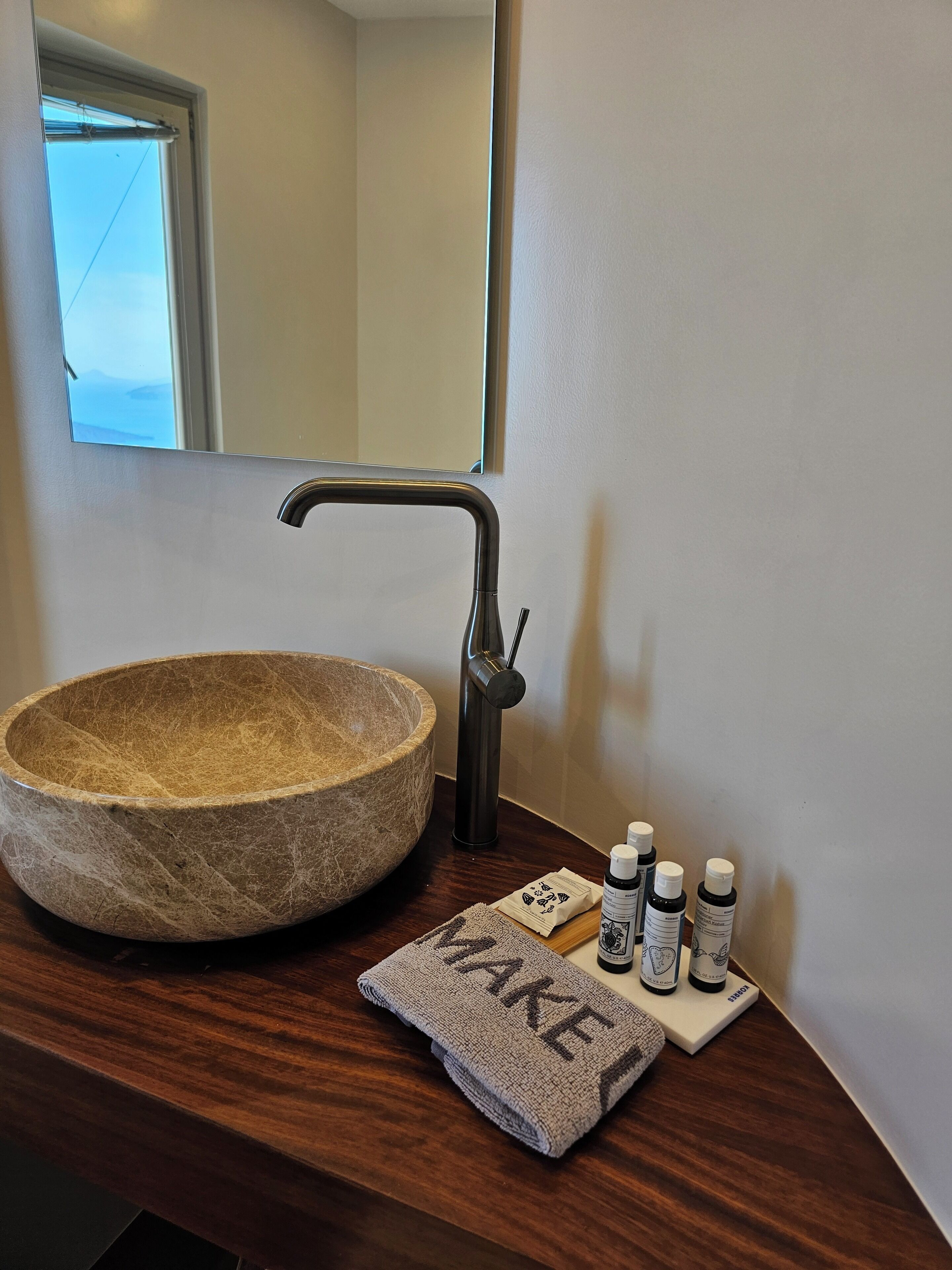 A bathroom with a stone basin, a modern faucet, and toiletries on the counter.