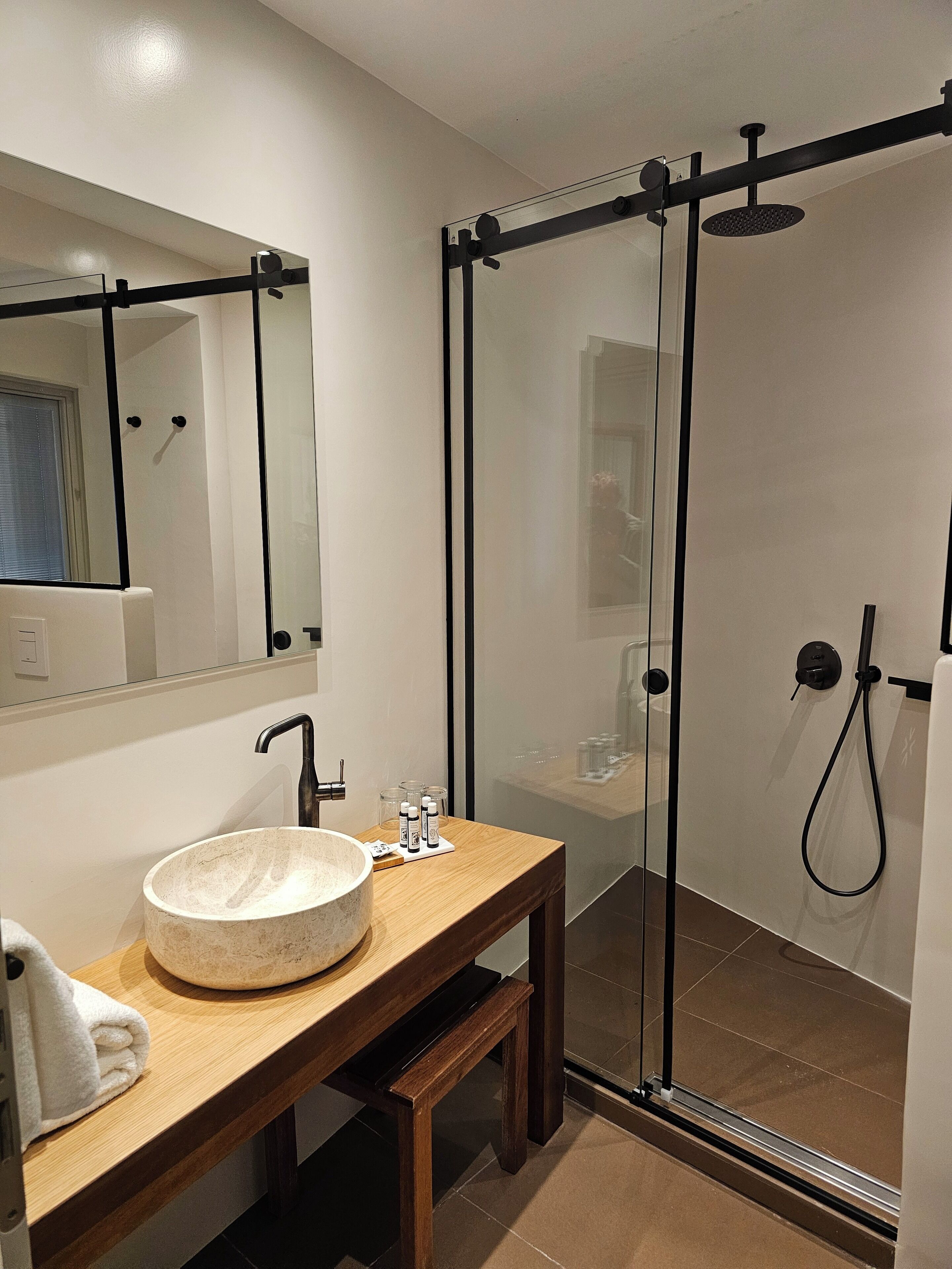 Un bagno moderno con un lavandino rotondo, uno specchio, un box doccia in vetro e un mobile bagno in legno.