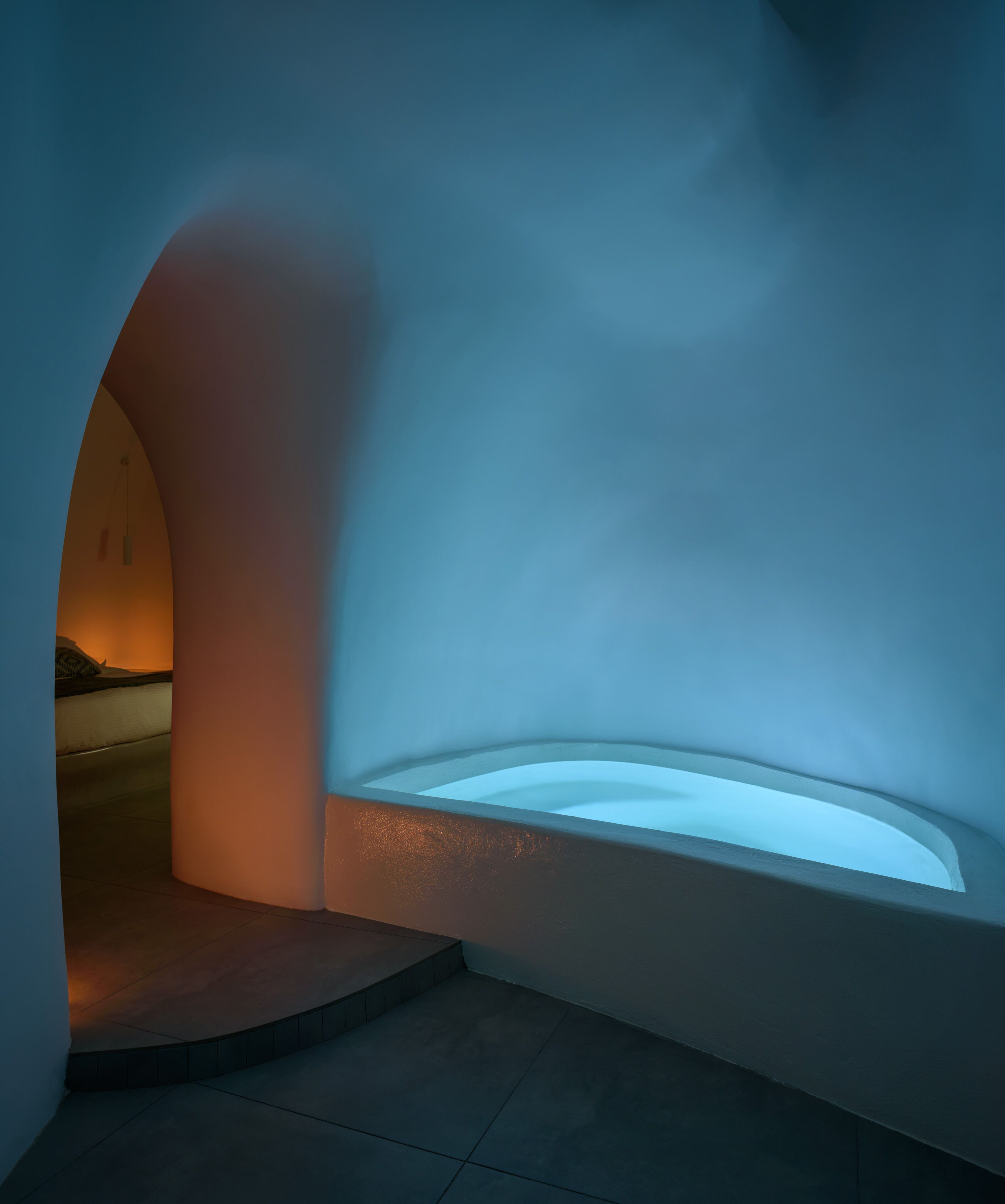 Un espacio arquitectónico moderno con un muro curvo y una zona hundida que parece ser de descanso o salòn.