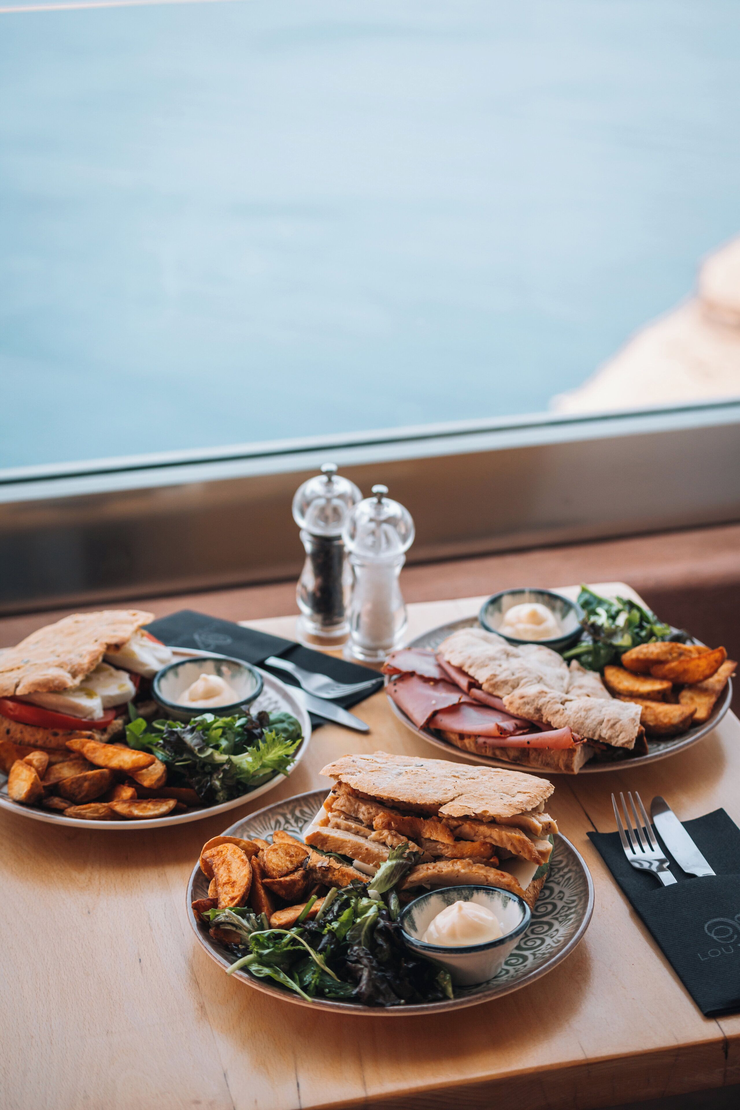 Une table où l’on voit un repas composé de sandwichs, de frites et d’une salade.