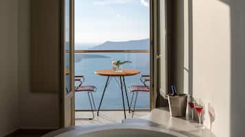 Ein Zimmer mit einer großen Badewanne, einem Tisch mit zwei Stühlen und Blick aufs Meer.