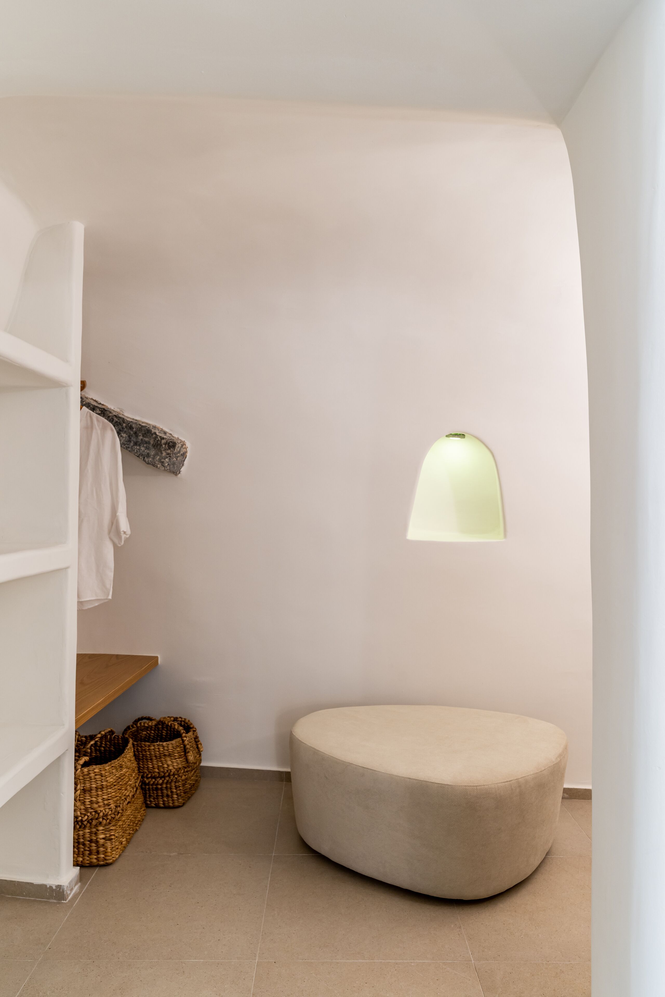 Quarto com decoração minimalista, um banquinho redondo, luminária pendente e cestos de palha no chão.