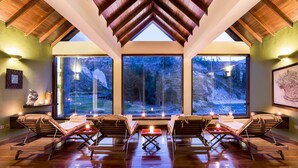 Un spa con vigas de madera en el techo, amplios ventanales con vistas a un paisaje montañoso y varias tumbonas con velas.