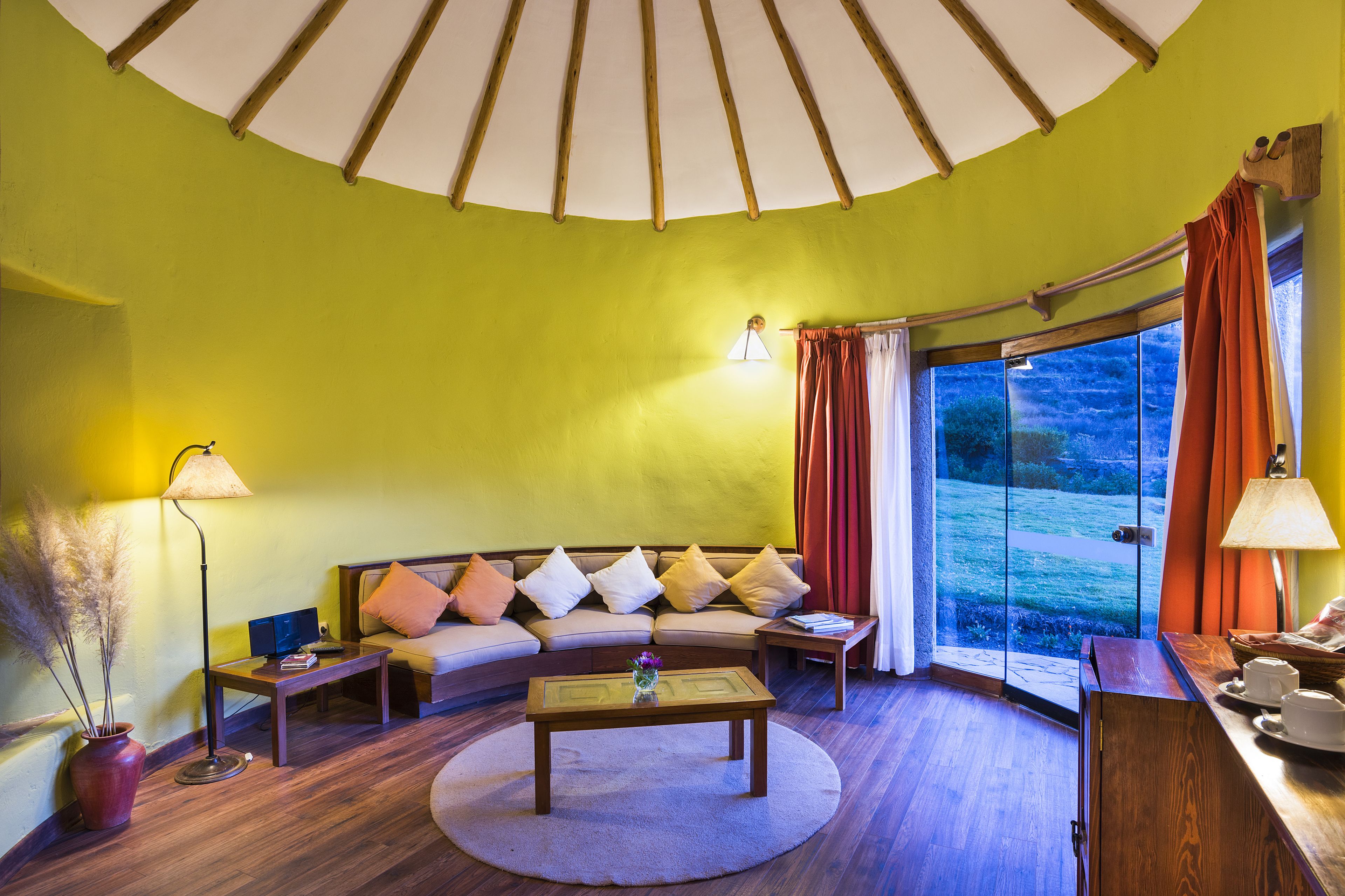 Una sala de estar acogedora con un sofá curvo, una mesa de centro y un ventanal con cortinas.