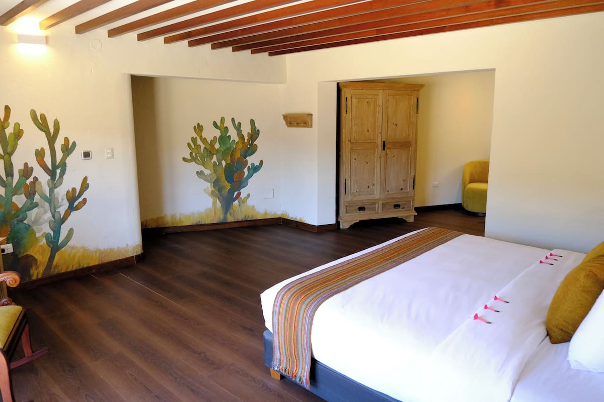 A bedroom with a wooden floor, a bed with a white and multicolored striped blanket, a wooden wardrobe, and a chair.