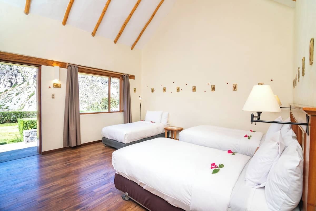 A hotel room with two beds, a wooden ceiling, a large window, and a view of the outdoors.