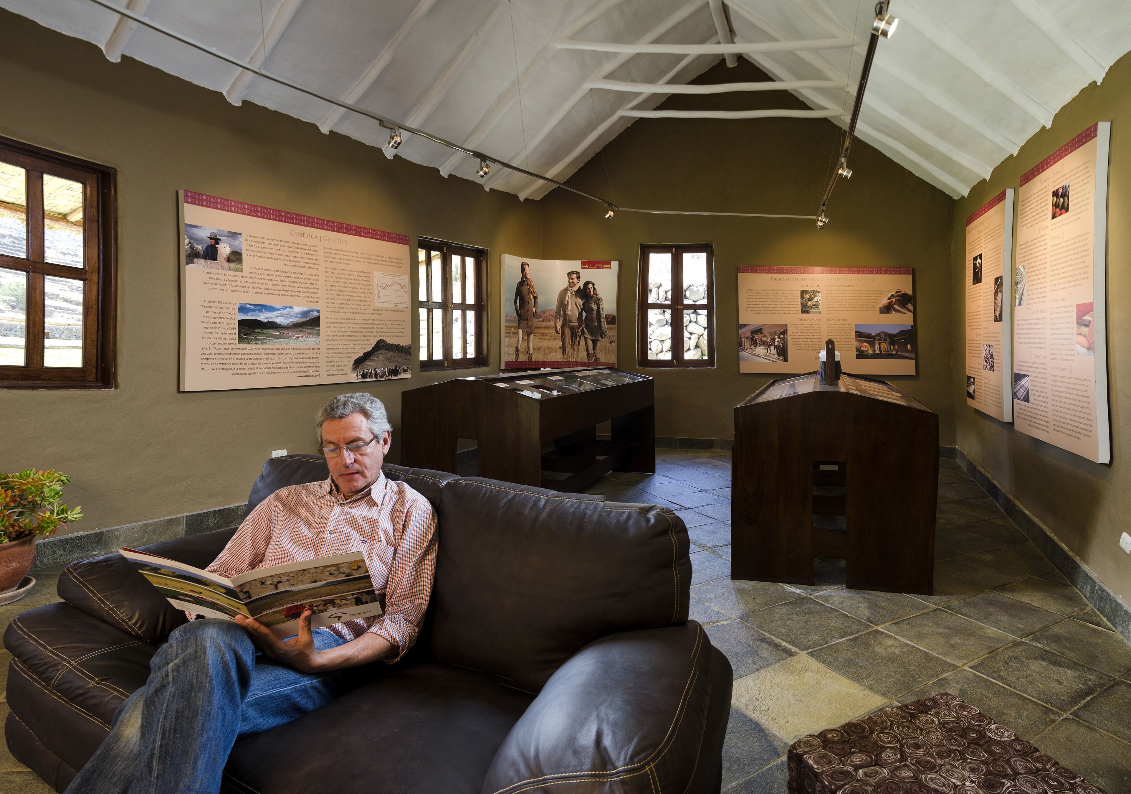 A man reading in a room with a high ceiling, large windows, and informational posters on the walls.
