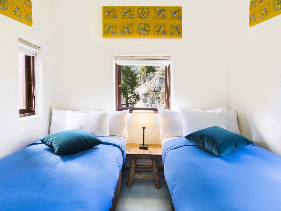 A room with two beds, a window with a view of trees and mountains, and a small table with a lamp.