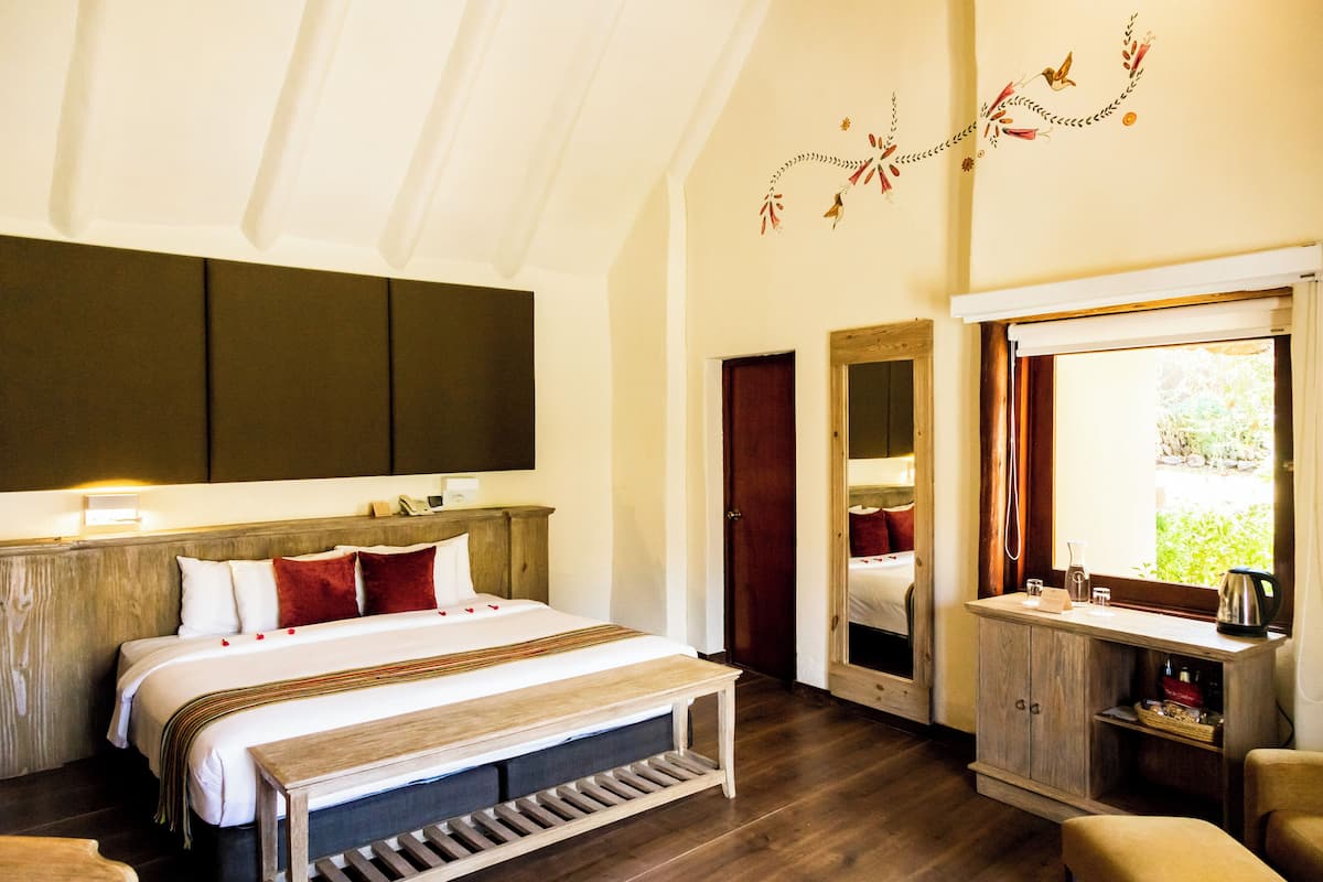 A bedroom with a large bed, a wooden bench, a bedside table, and a mirror.