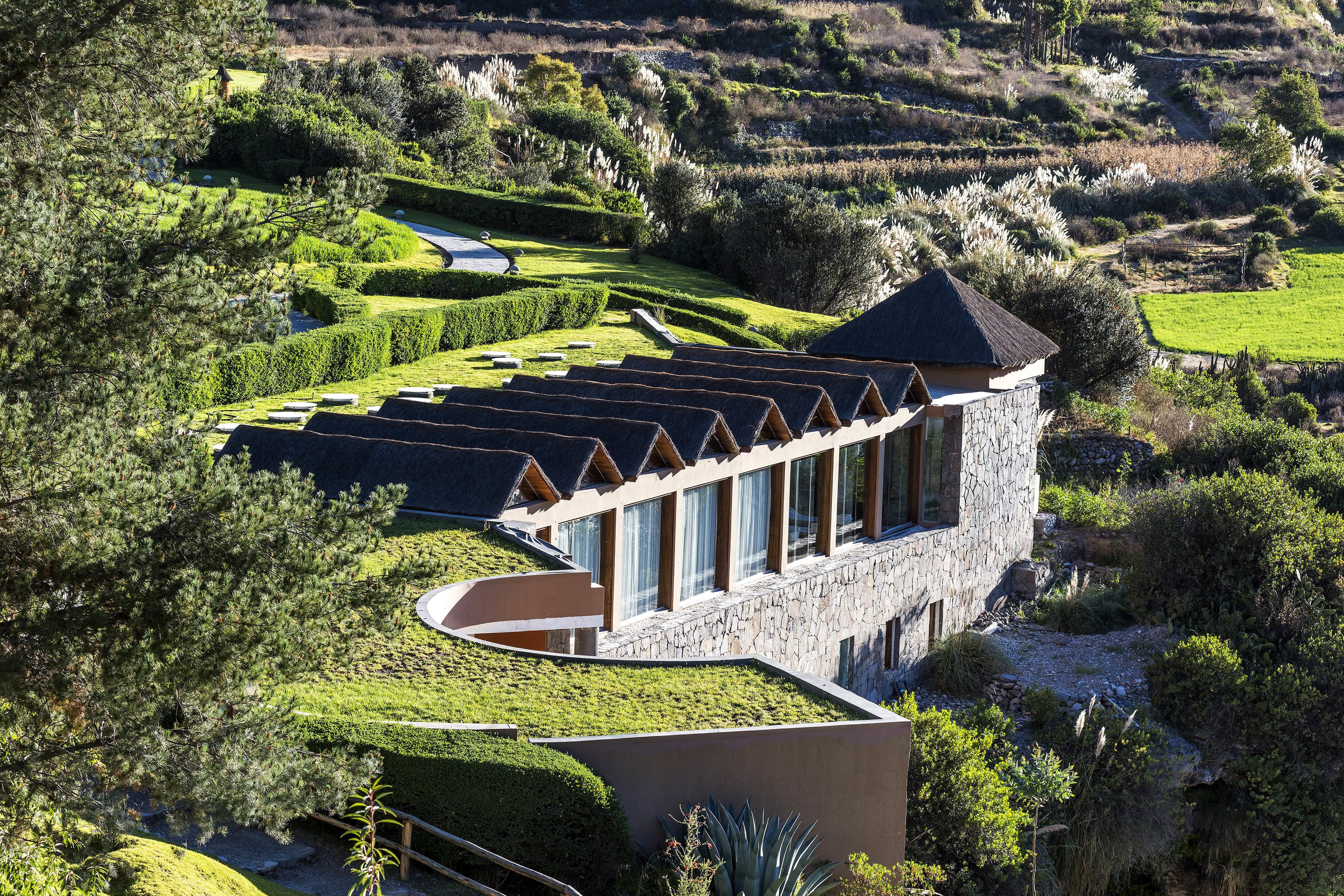 A modern building with a curved roof, surrounded by well-maintained gardens and terraced fields.