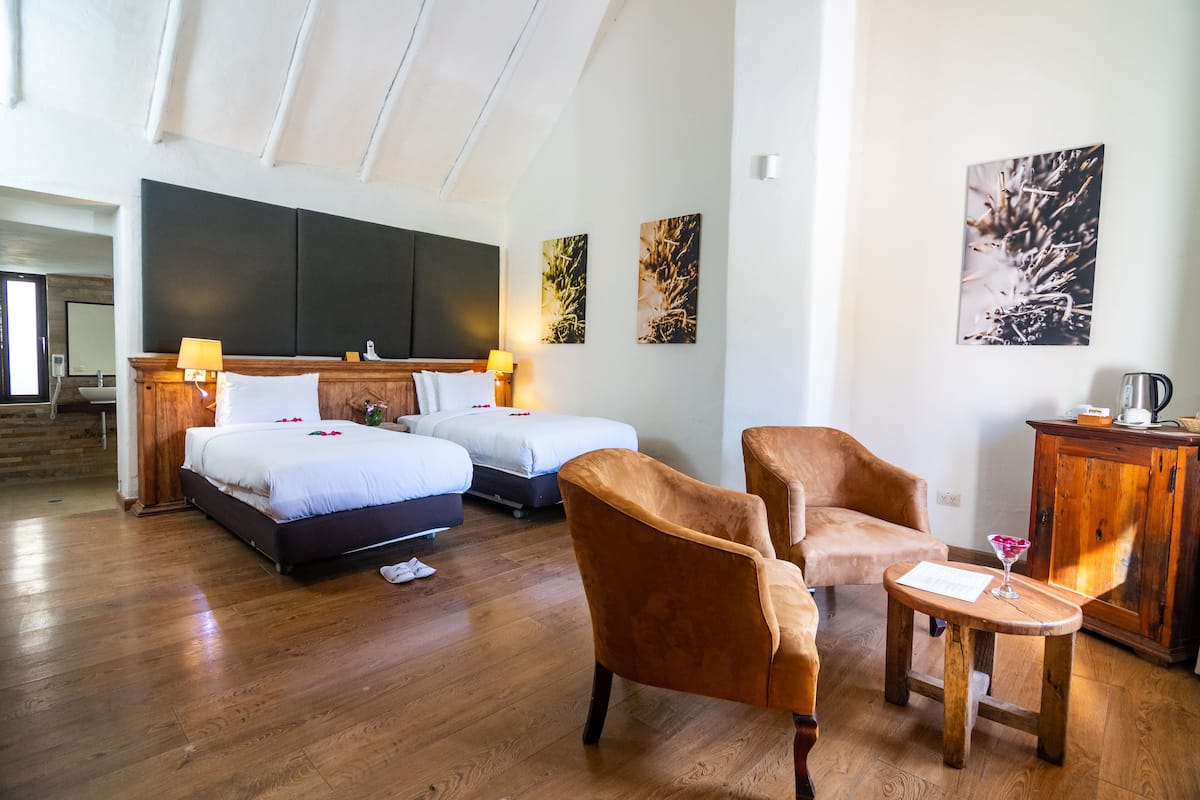 A hotel room with two beds, a wooden headboard, a wooden cabinet, and a small table with a glass.
