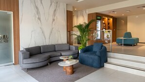Un hall d’entrée moderne avec un canapé d’angle gris, un fauteuil bleu, un mur en marbre, un mur avec un panneau en bois et une cloison en verre.