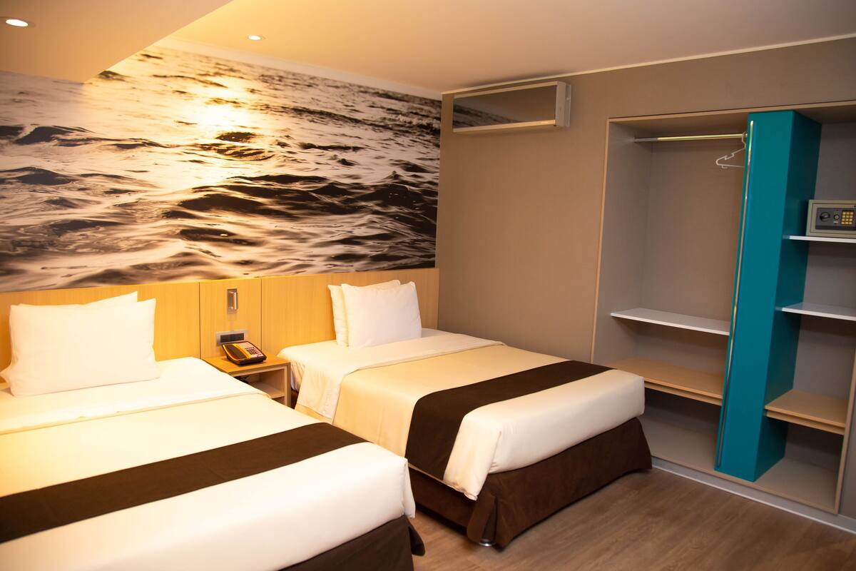 Une chambre d’hôtel avec deux lits, une fresque murale, une armoire et une petite table de chevet.