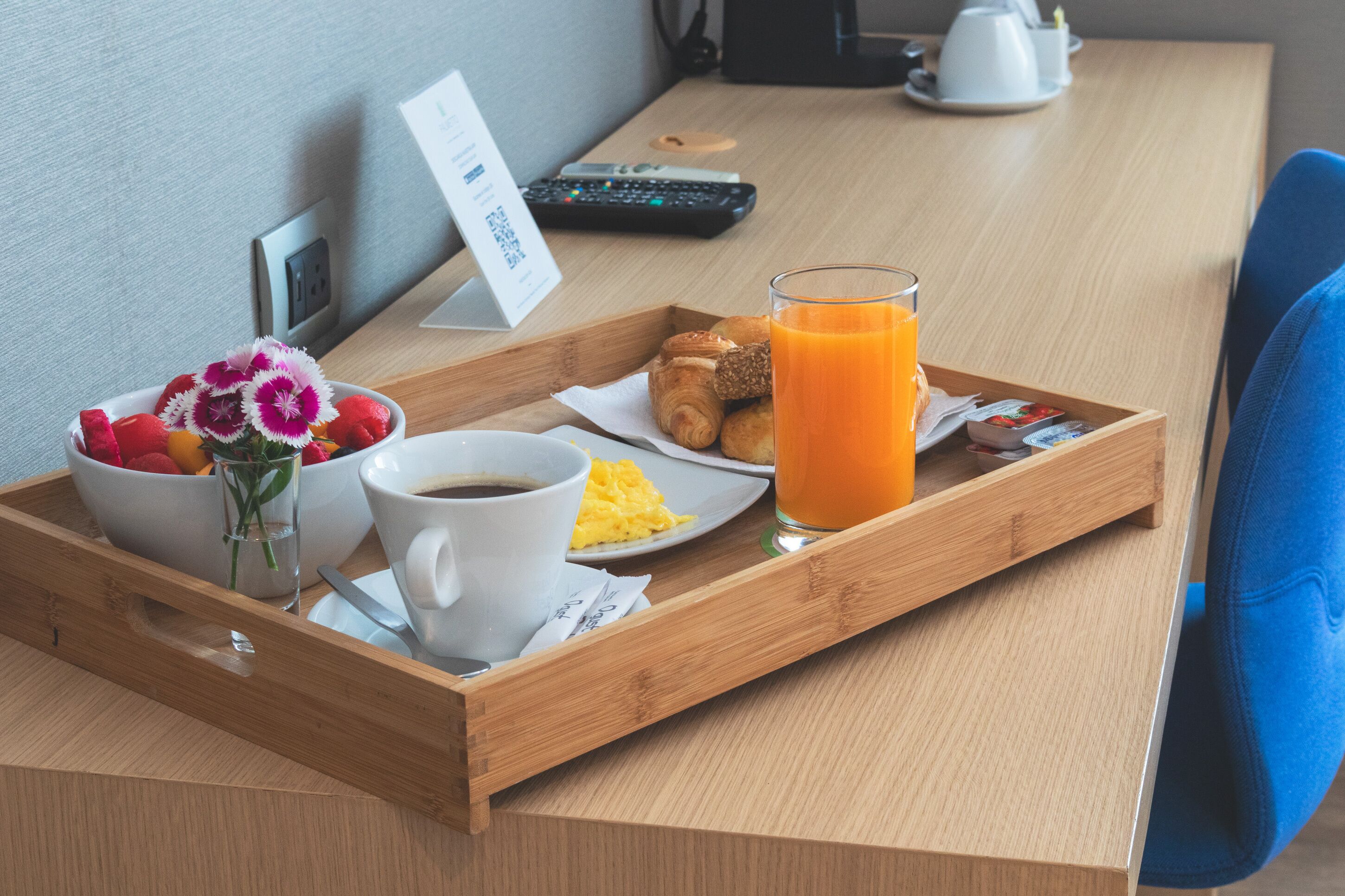 Bandeja de desayuno con croissants, huevos revueltos, café y jugo de naranja sobre una mesa de madera.