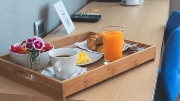 Bandeja de desayuno con croissants, huevos revueltos, café y jugo de naranja sobre una mesa de madera.