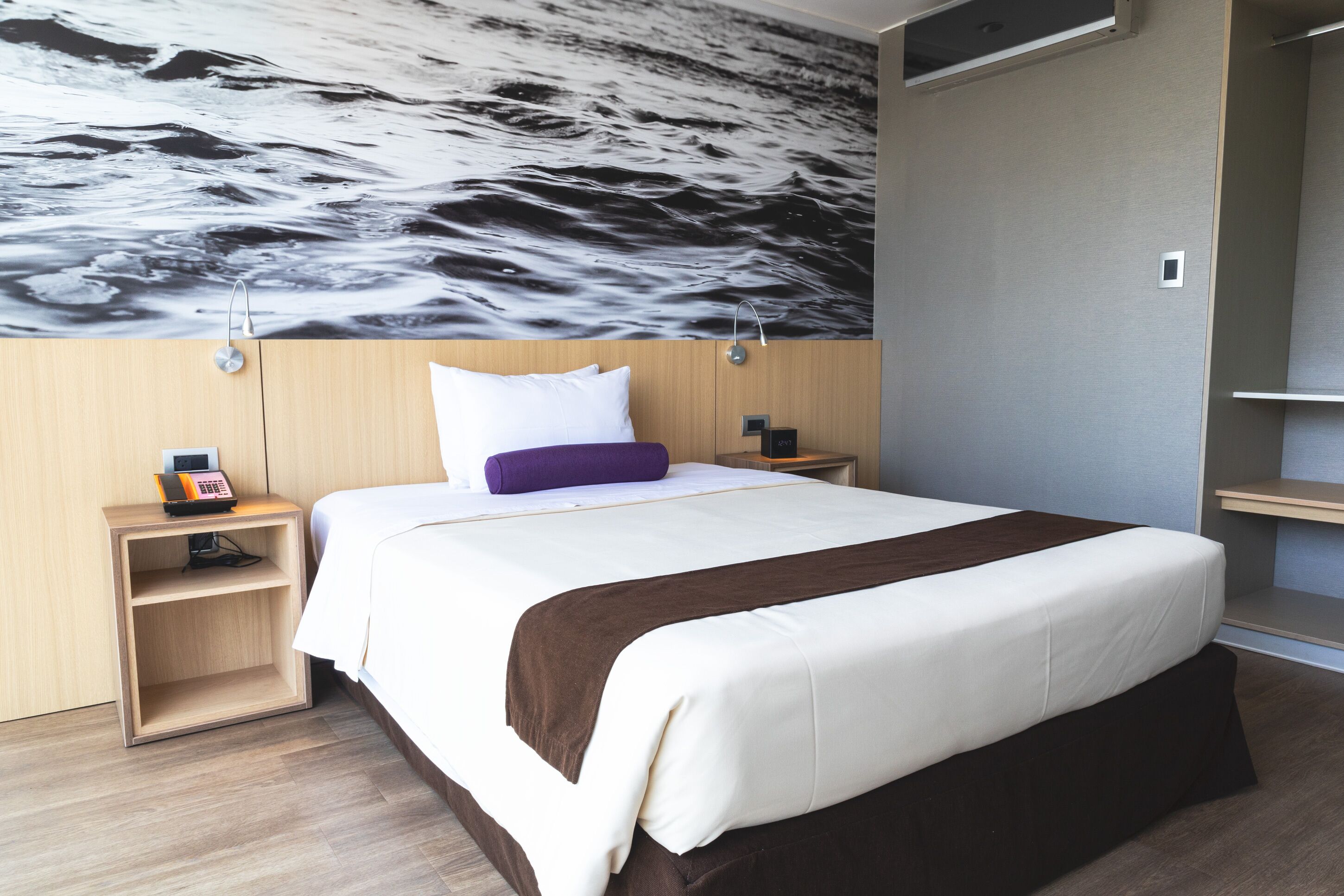 A modern hotel room with a large bed, a nightstand with a phone, and a wall mural.