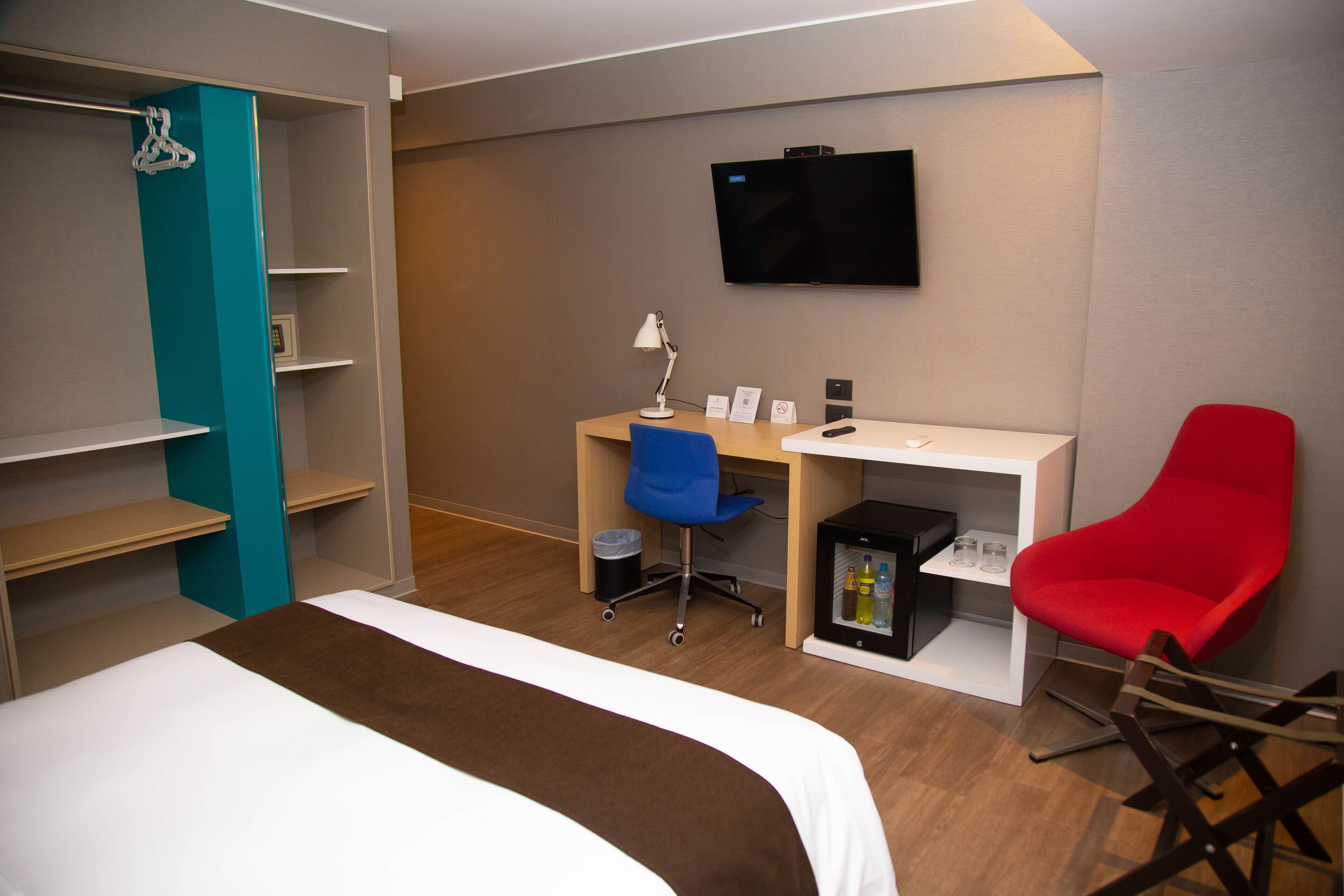 Hotellihuone, jossa on sänky, työpöytä tuolilla, televisio ja minibaari.