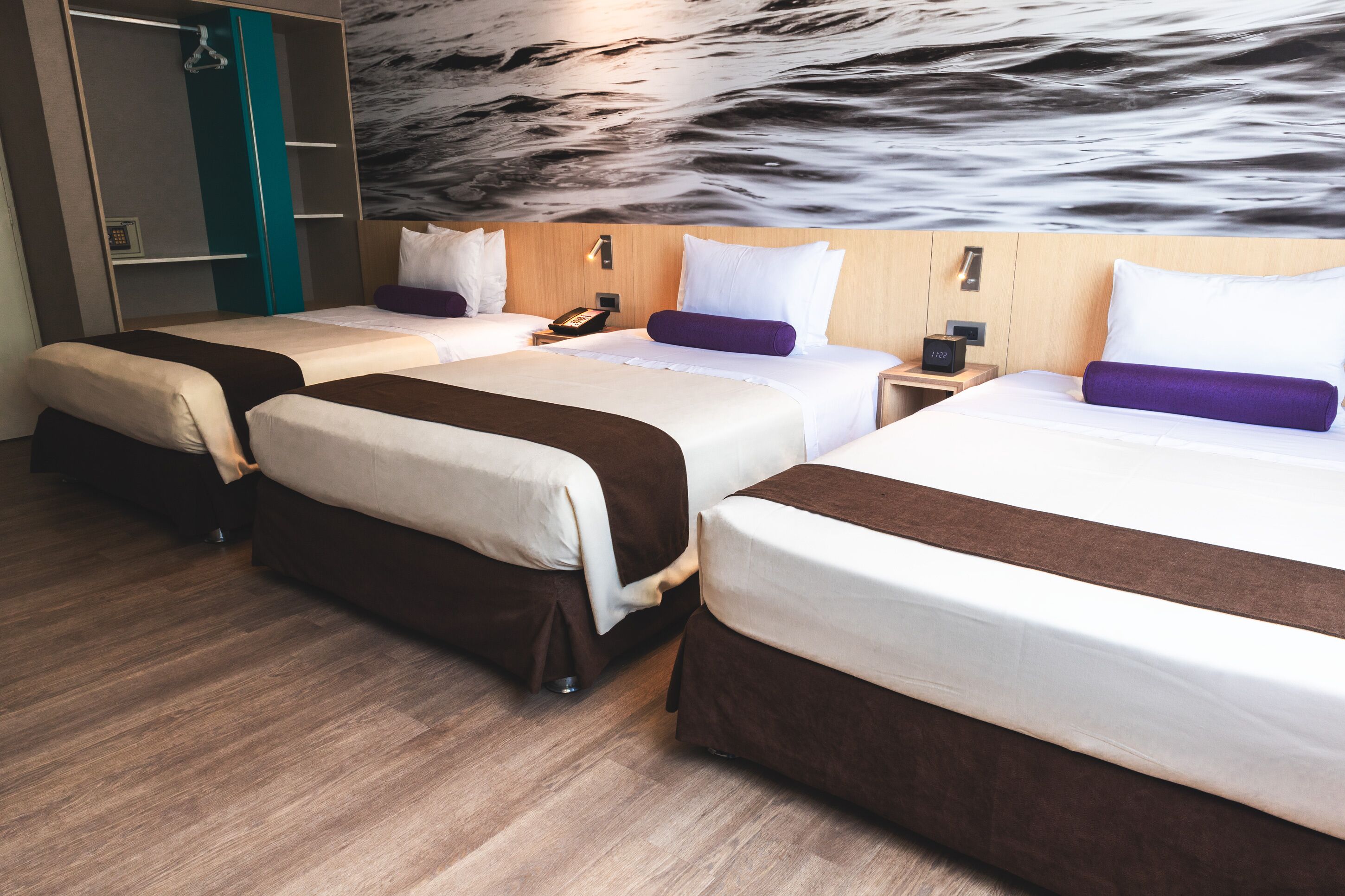 A hotel room with three beds, a wooden floor, and a wall mural.