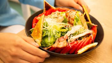 Uma pessoa segurando uma tigela de salada com alface, tomate e queijo ralado.