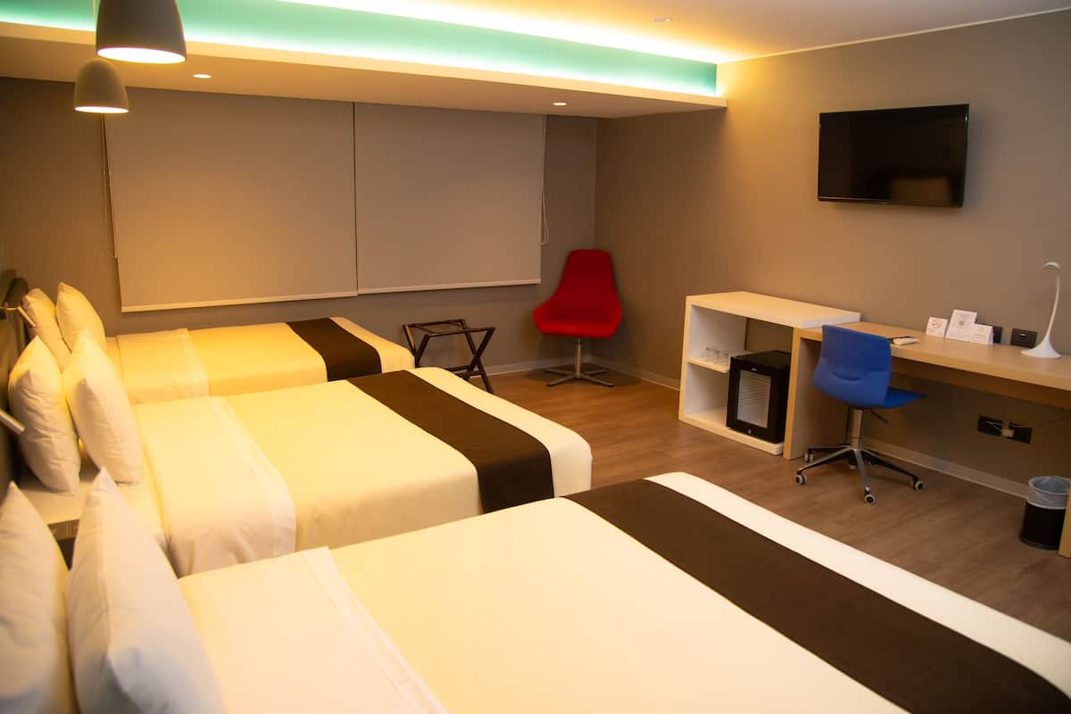 Une chambre d’hôtel avec deux lits, un bureau, une chaise rouge, une télévision et une petite poubelle.
