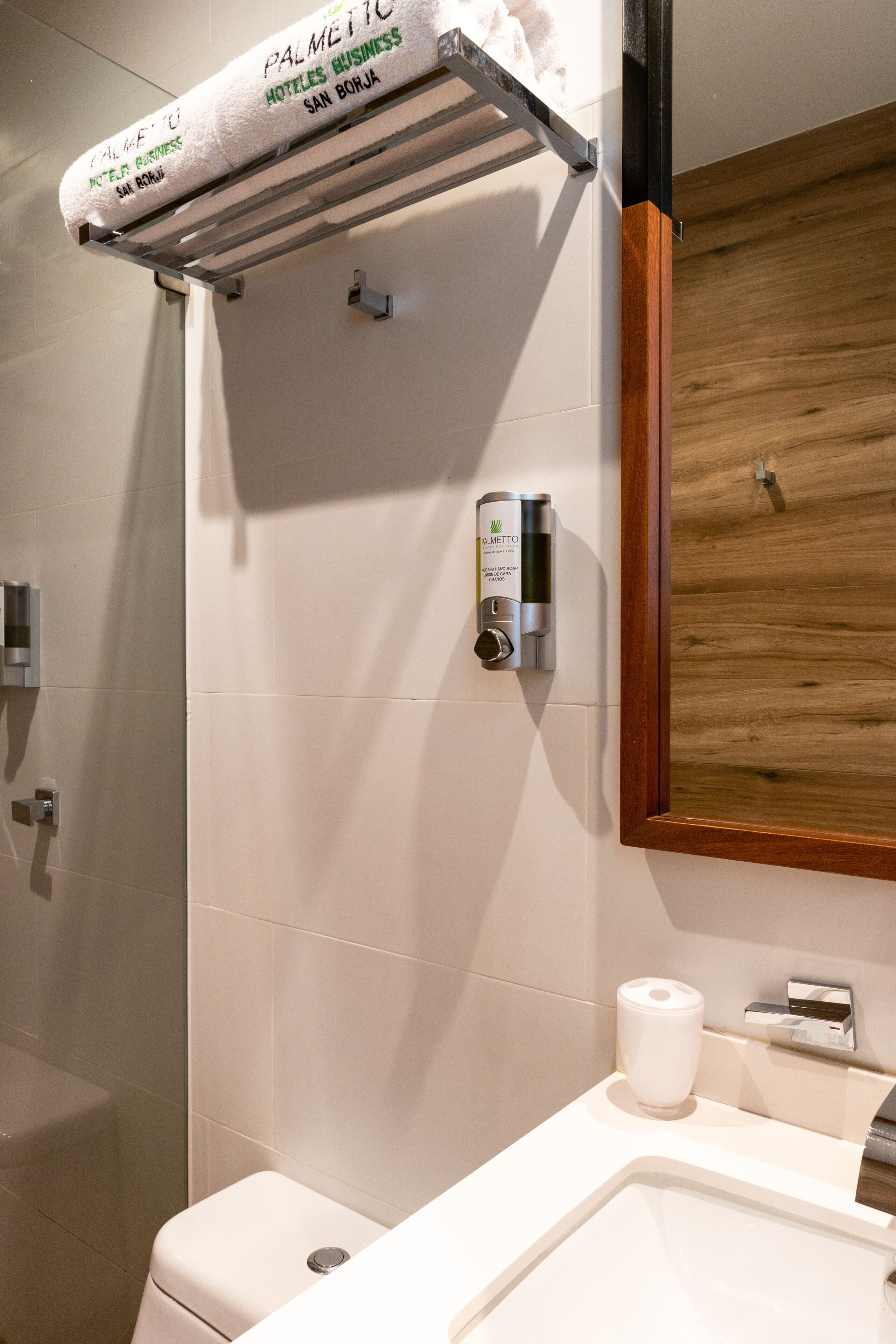 A bathroom with a toilet, a sink, a mirror, a towel rack with a towel, and a soap dispenser.