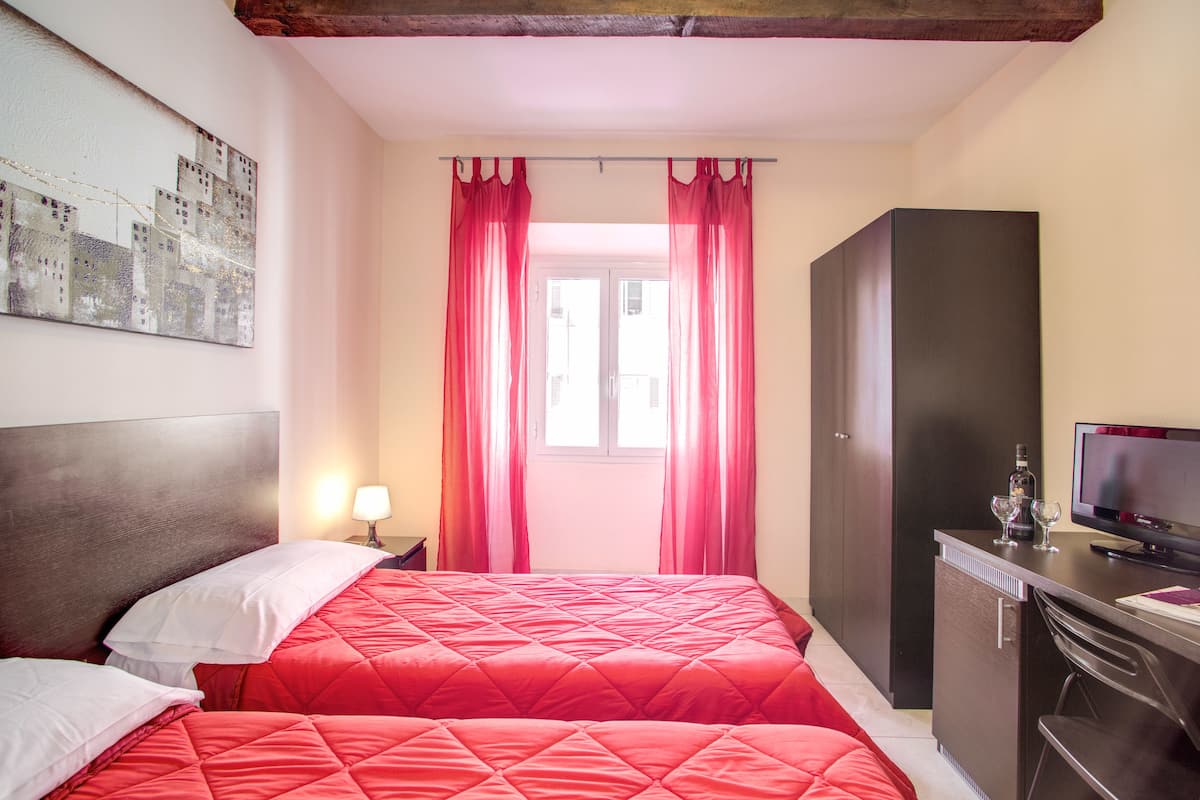 A hotel room with two beds, a desk with a TV, and a window with curtains.