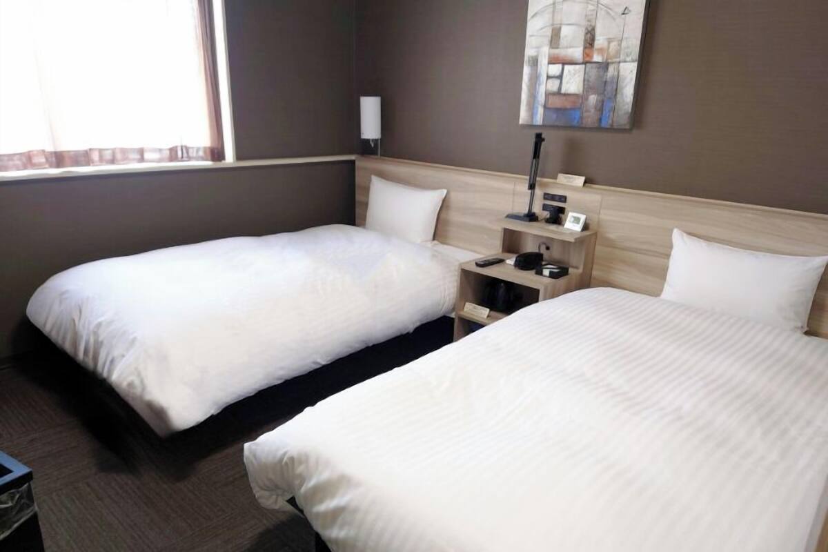 A hotel room with two beds, a bedside table, a lamp, and a painting on the wall.