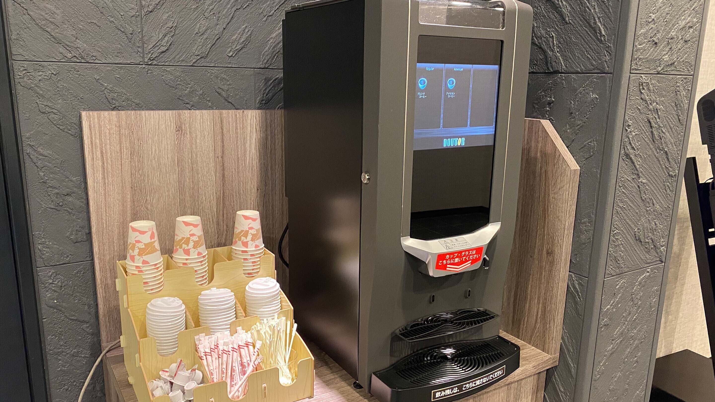 A self-service beverage dispenser with a digital screen, a cup holder, and a tray for cups and straws.