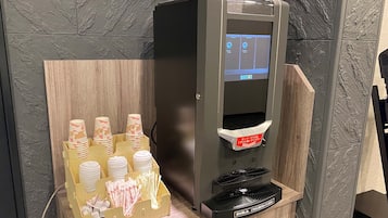 A self-service beverage dispenser with a digital screen, a cup holder, and a tray for cups and straws.