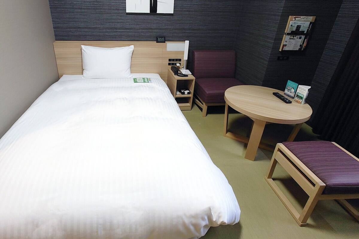 A hotel room with a bed, a desk, a chair, and a small table.