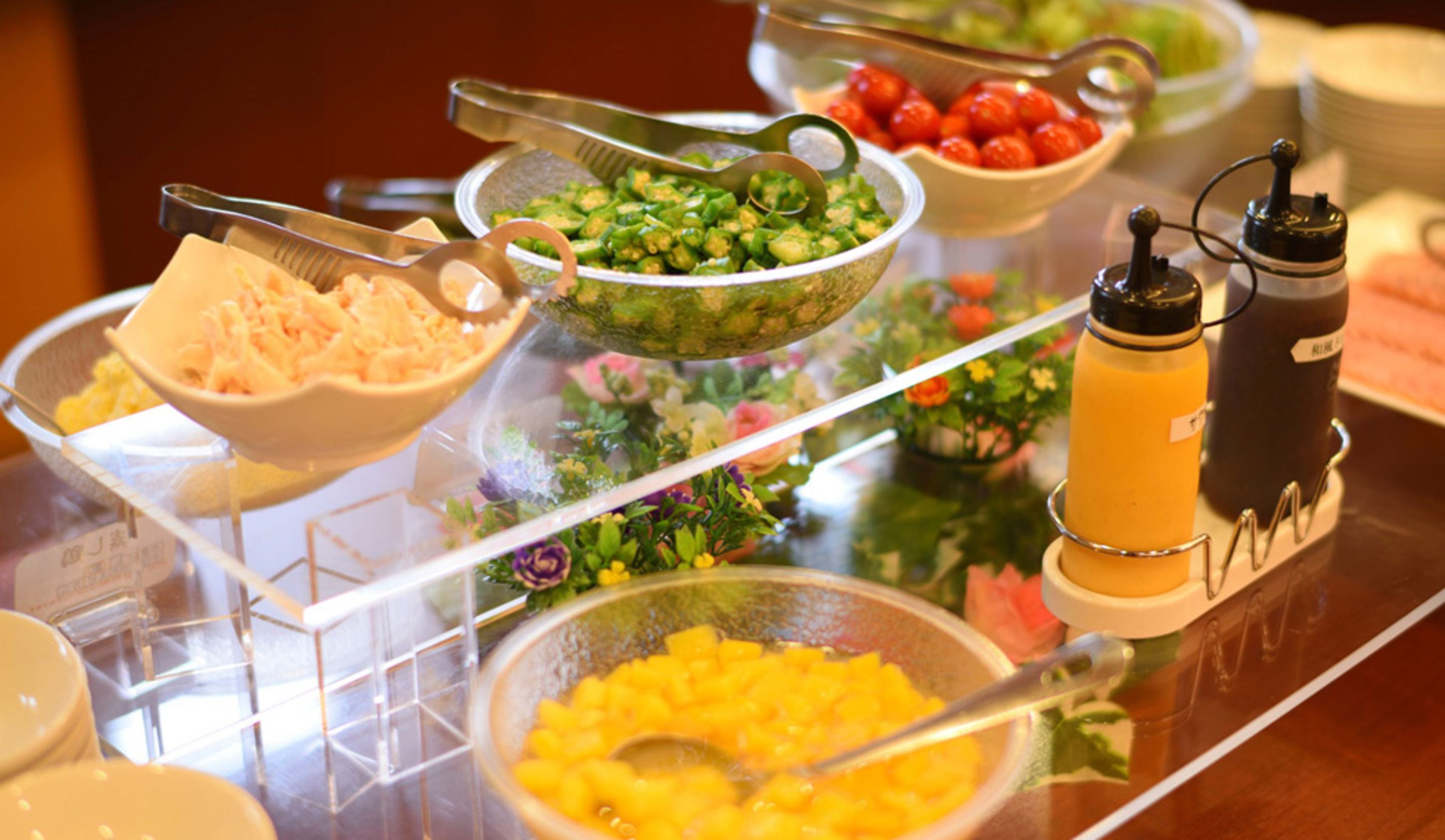 Een buffet met diverse soorten eten, waaronder geraspte kaas, groene groenten, tomaten en een geel drankje.