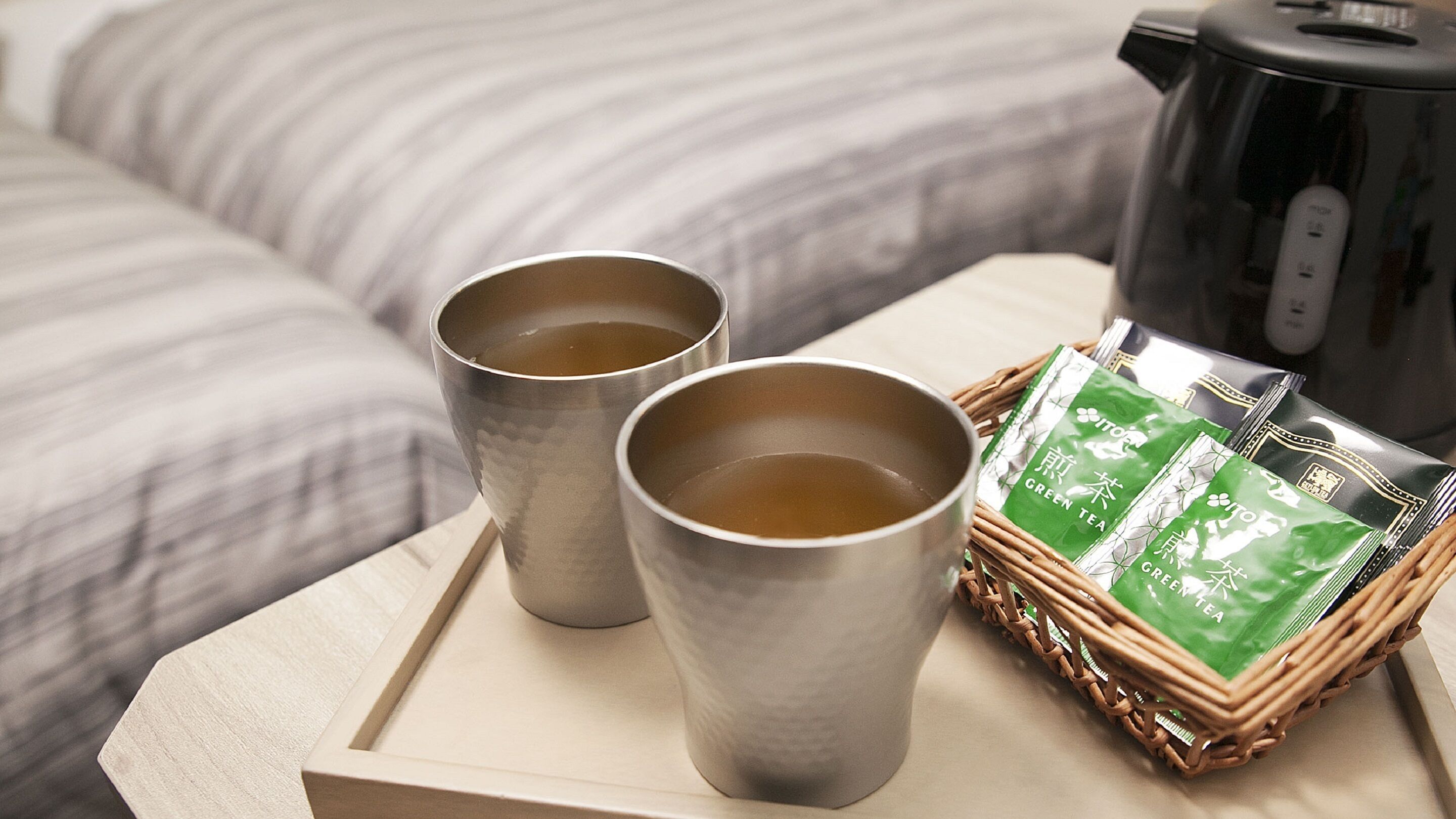 Two metal cups on a tray, a green tea package, and a black kettle on a table.