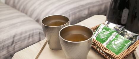 Two metal cups on a tray, a green tea package, and a black kettle on a table.
