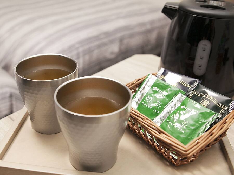 Two metal cups on a tray, a green tea package, and a black kettle on a table.