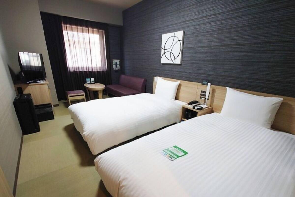 A hotel room with two beds, a desk, a chair, a TV, and a window with curtains.