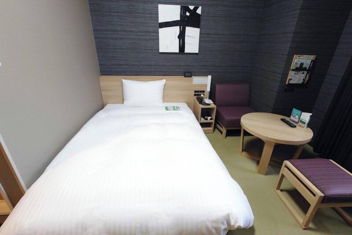 A hotel room with a bed, a small desk, a chair, a round table, and a wall-mounted artwork.