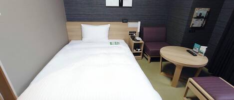 A hotel room with a bed, a small desk, a chair, a round table, and a wall-mounted artwork.