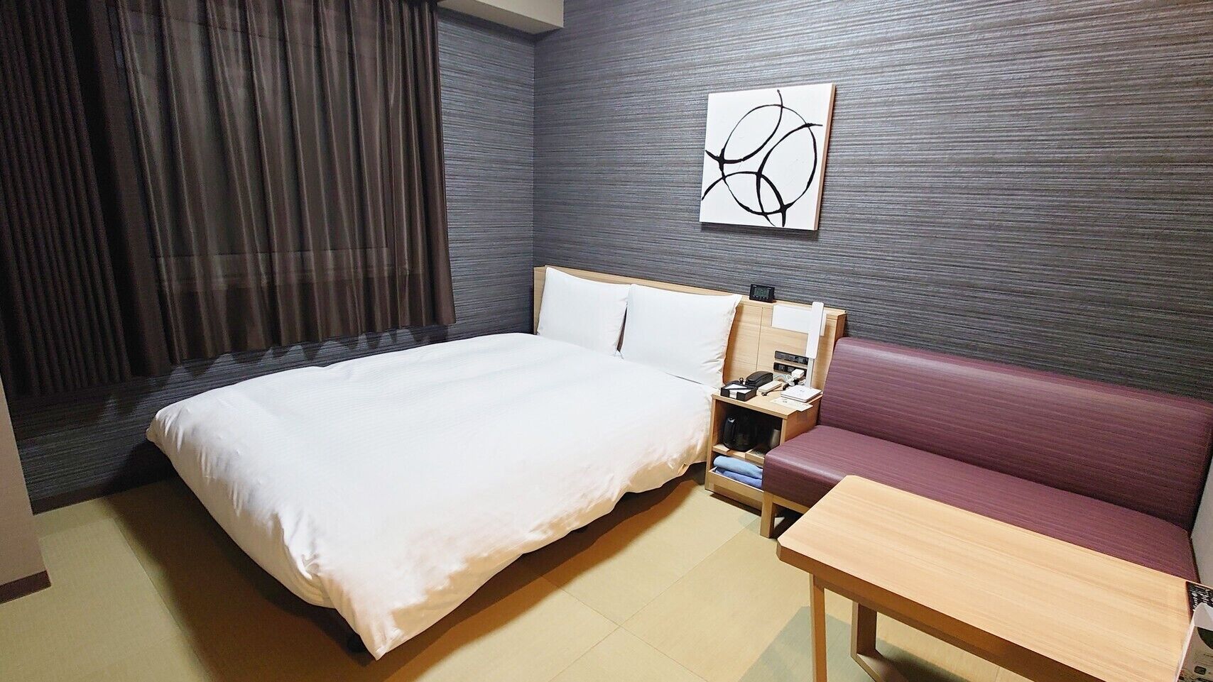 Een hotelkamer met een bed, nachtkastje, een slaapbank en een kunstwerk aan de muur.