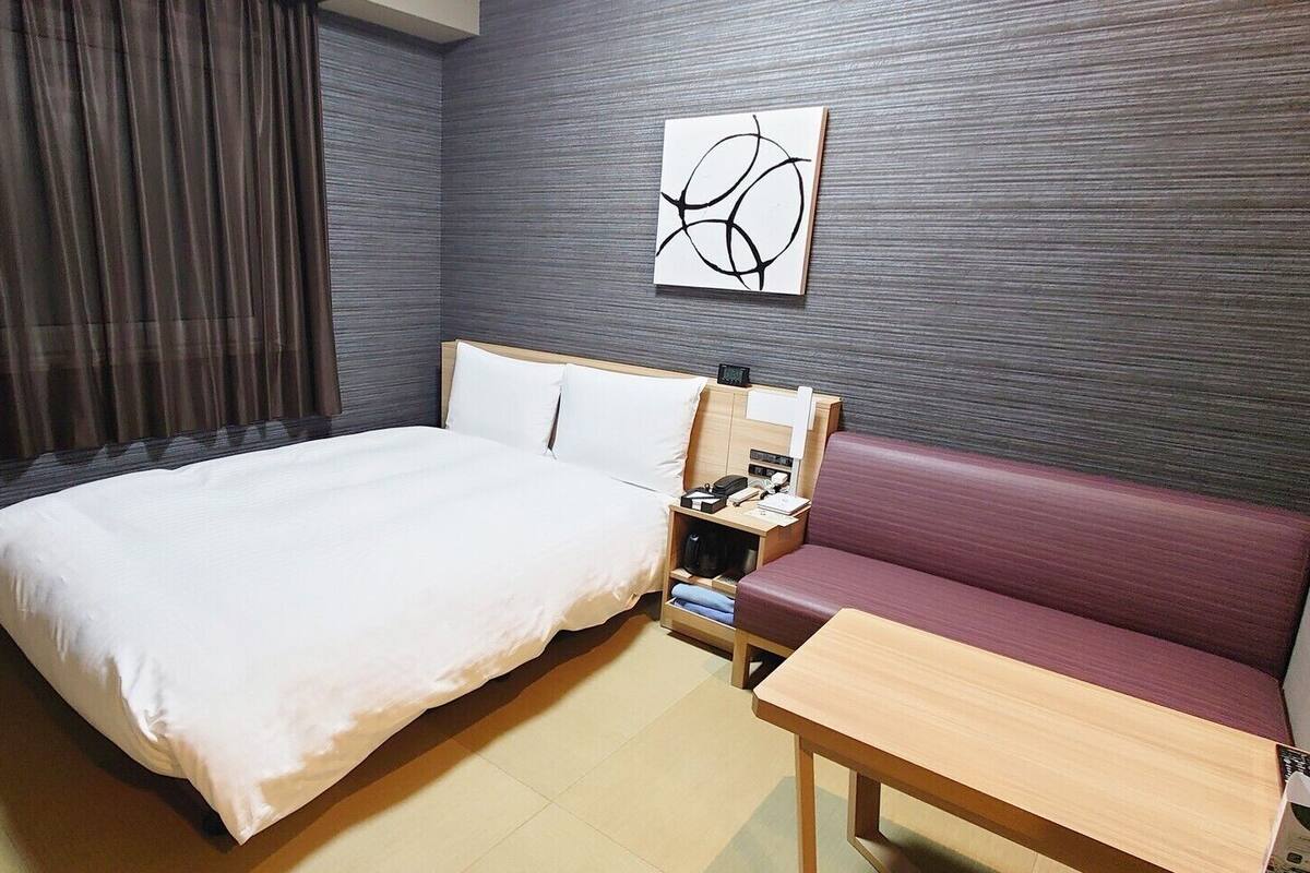 A hotel room with a bed, a bedside table, a nightstand, a sofa, and a wall-mounted artwork.