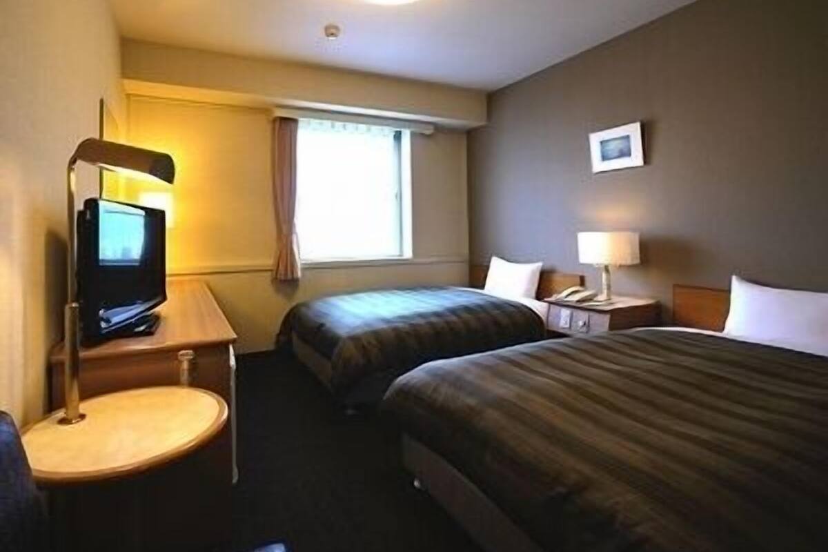 A hotel room with two beds, a desk with a television, a lamp, and a small picture on the wall.