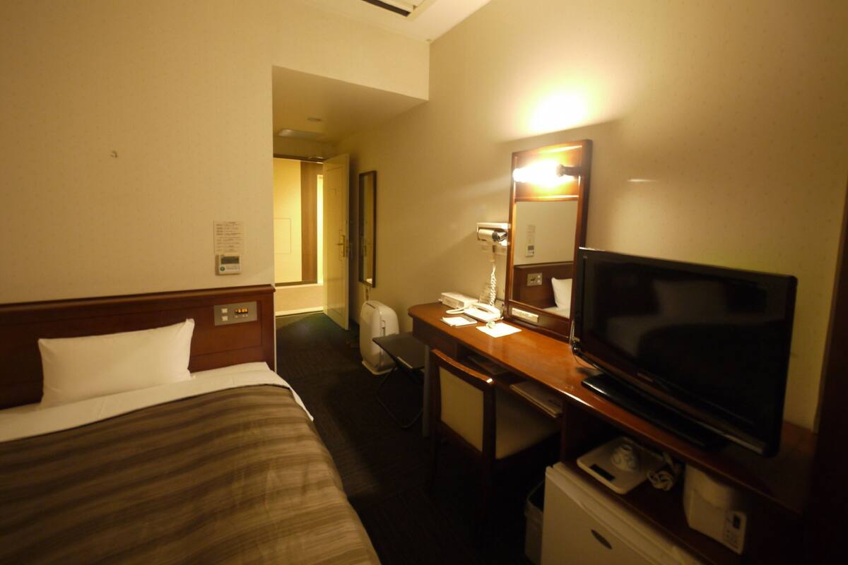 A hotel room with a bed, a desk with a TV, a mirror, a hairdryer, and a scale.