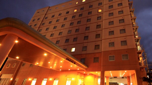 A multi-story hotel with a modern design, featuring a prominent entrance with a curved roof and multiple illuminated windows.