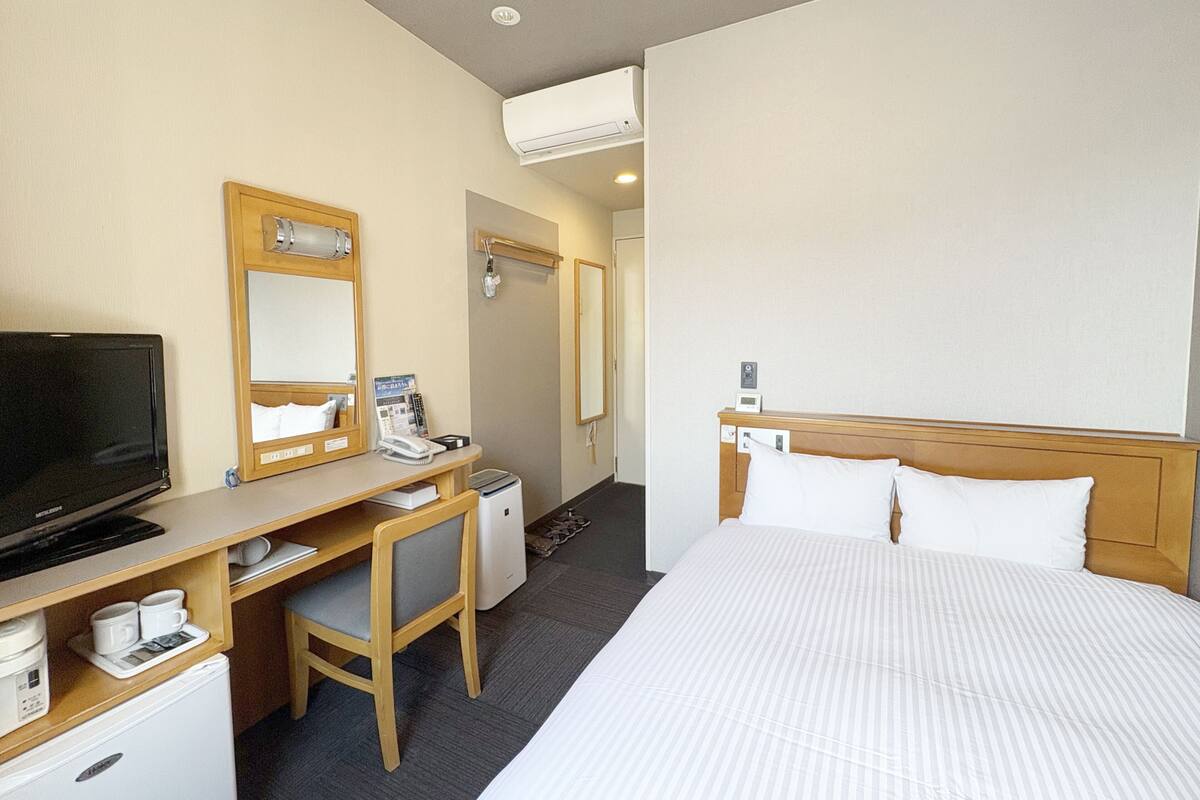 A hotel room with a bed, a desk with a computer, a television, a mini-fridge, a microwave, and a small refrigerator.