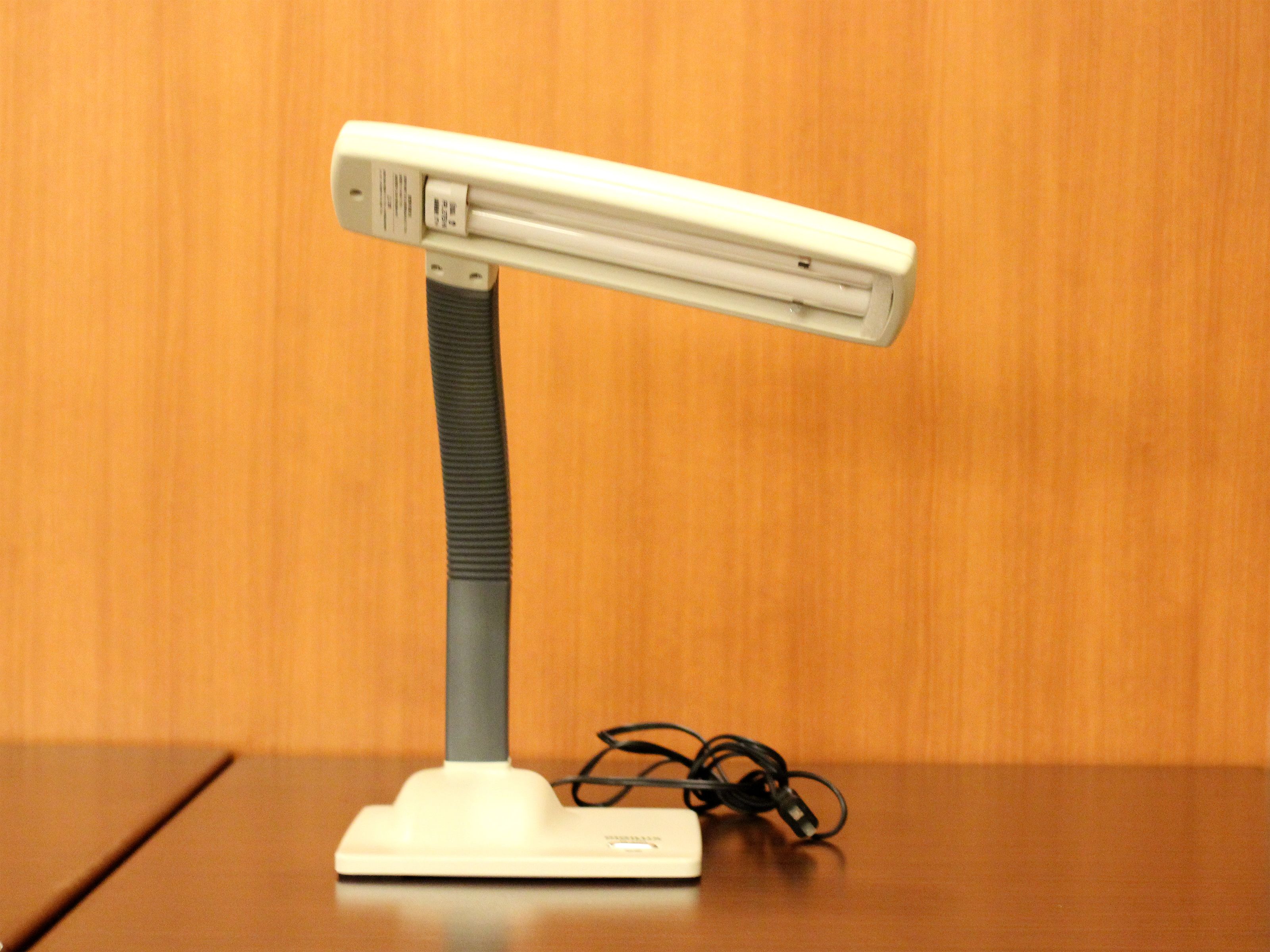 A white desk lamp with a flexible neck and a power cord on a wooden table.