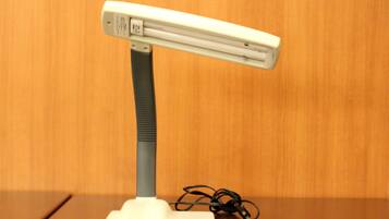 Una lámpara de escritorio blanca con cuello flexible y un cable de alimentación sobre una mesa de madera.