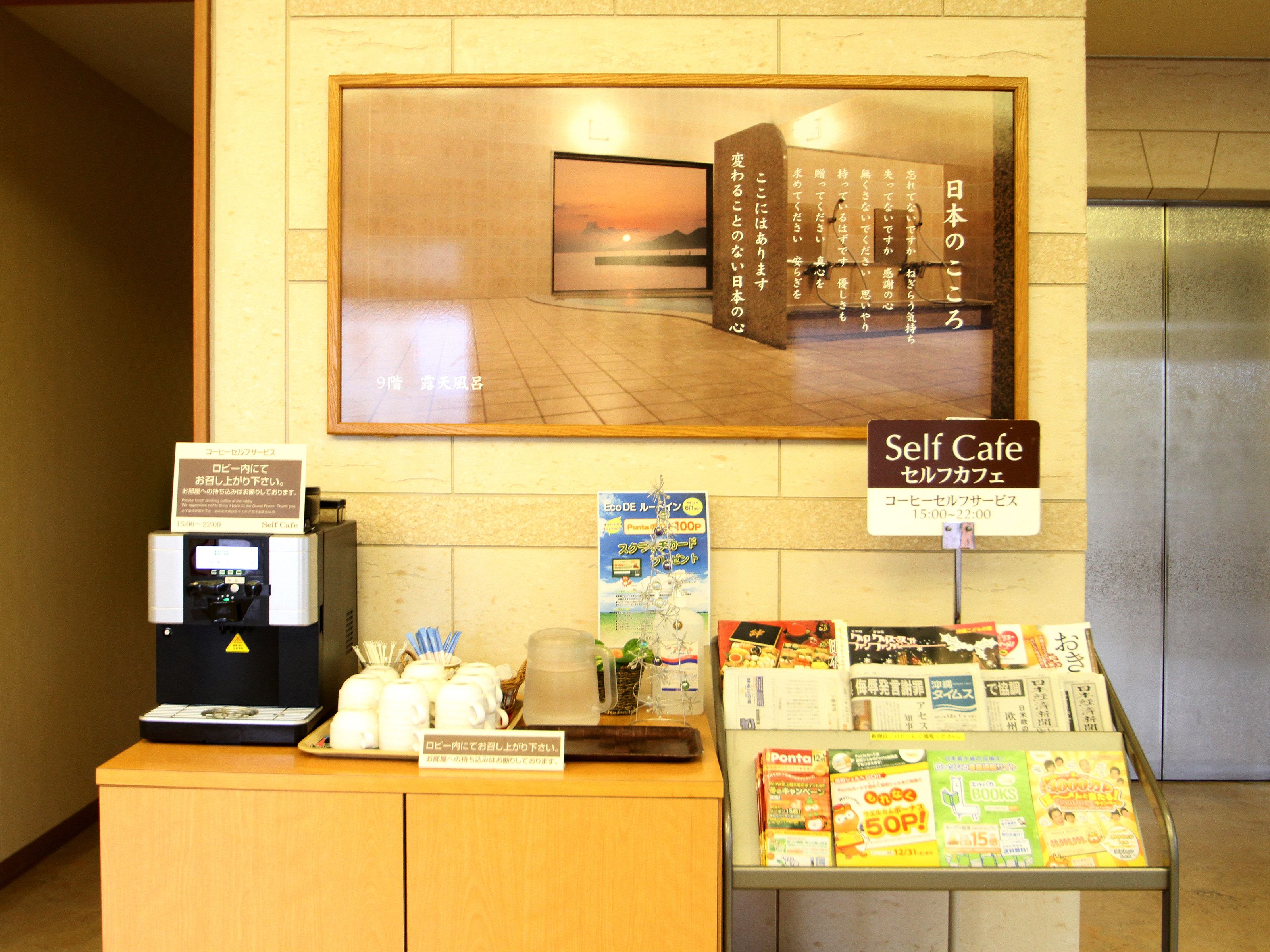 A self-service coffee station with a coffee machine, cups, and a display of books and magazines.