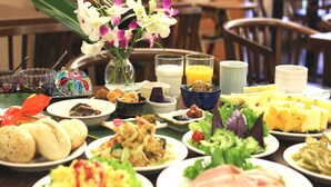 A table with various dishes, including salads, meats, and fruits, along with a vase of flowers and some drinks.