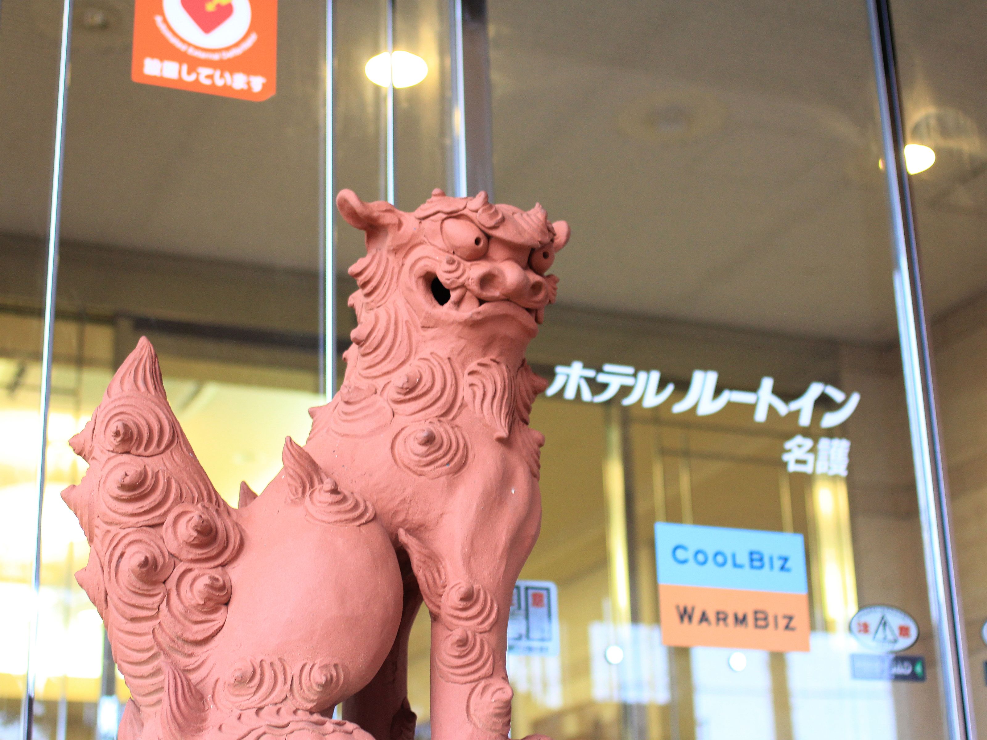A pink ceramic lion statue in front of a glass window with signs reading "CoolBiz" and "WarmBiz".